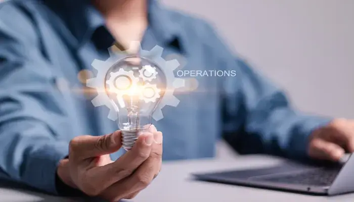 A person holding a lit bulb with gears inside, symbolizing operational excellence and innovation.