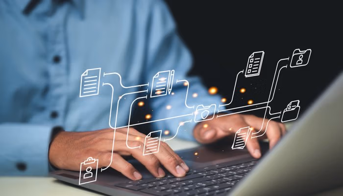 A person typing on a laptop with virtual icons of documents and folders, representing enterprise asset management.