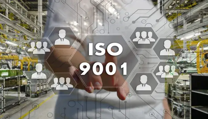 A person pointing to a virtual interface displaying "ISO 9001" in a factory setting, representing Quality Management Systems (QMS)