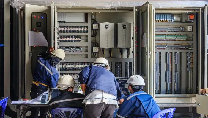 Engineers in hard hats working on electrical panels, discussing maintenance strategies