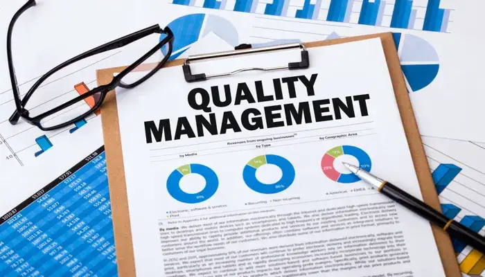 Clipboard with a Quality Management report, charts, graphs, and glasses, illustrating QMS in manufacturing.