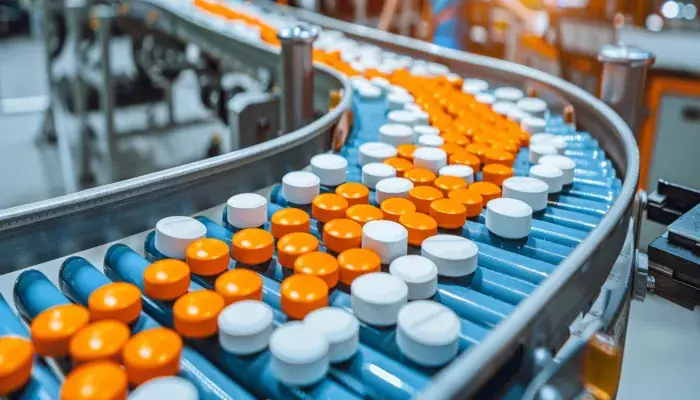 A conveyor belt in a pharmaceutical factory transports white and orange pills, illustrating a quality management system in pharma.