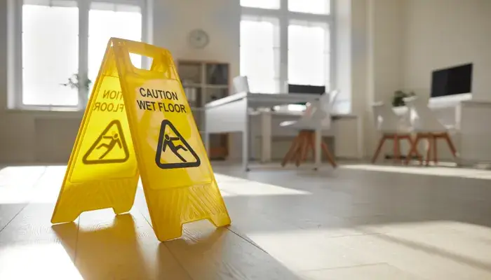 A yellow "Caution Wet Floor" sign stands prominently in an office space, highlighting workplace injury prevention measures.