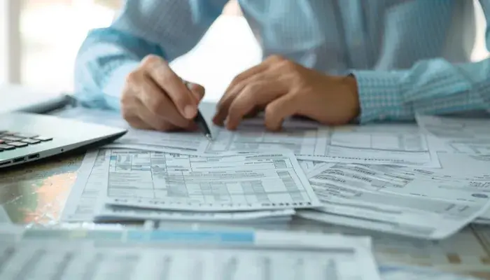 A person in a blue shirt reviews and annotates numerous documents on a desk, exemplifying documentation best practices.