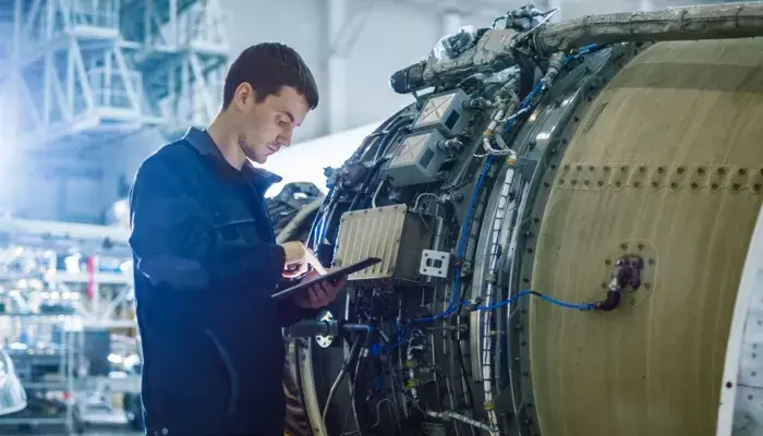 Engineer performing predictive maintenance on aircraft engine using a digital tablet.