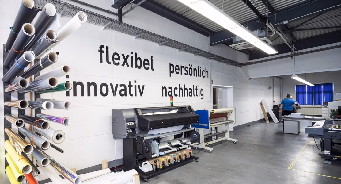Modern printing workshop with rolls of printing material on racks and large industrial printers