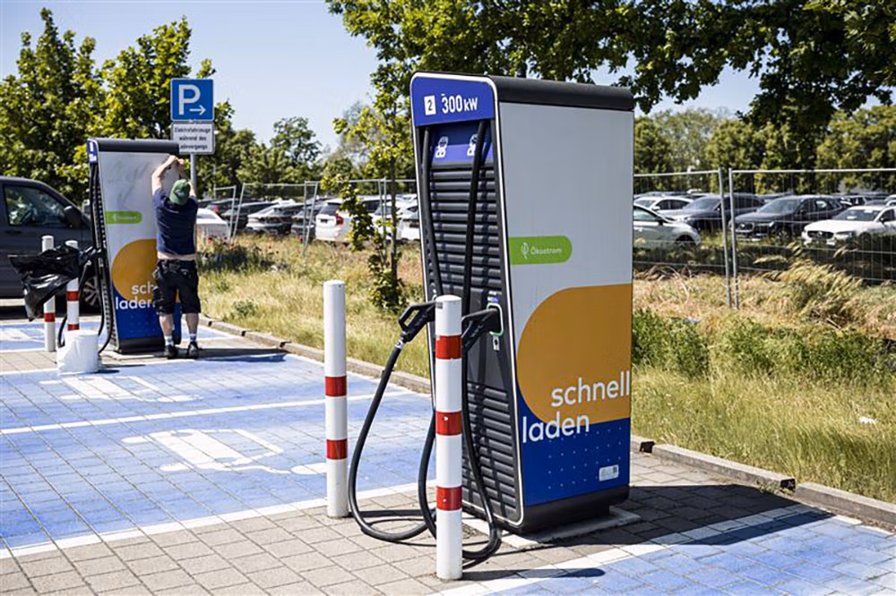 Two fast electric vehicle charging stations in a parking lot with one person adjusting signage nearby.