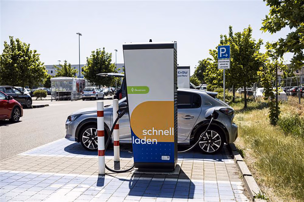 Silver electric car charging at a fast charger station labeled “schnell laden” in a sunny outdoor parking