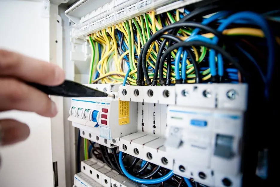 Close-up of a hand operating a circuit breaker inside an electrical panel with colored wires visible.